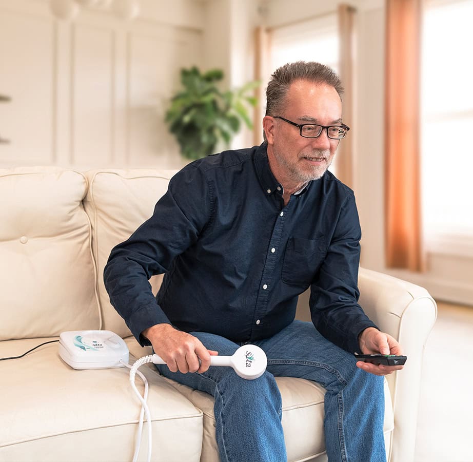 A man relaxing on a couch, using the Magnetic Pulser Hand Paddle while watching TV