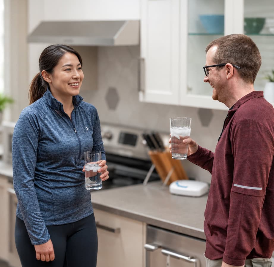 A couple in a kitchen, holding glasses of ozonated water and smiling